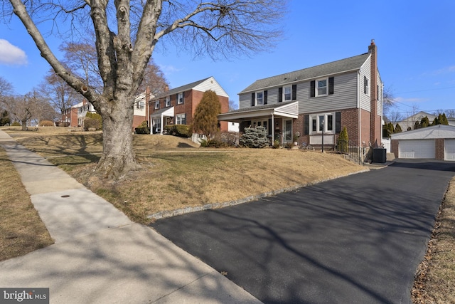 colonial-style house with an outbuilding, brick siding, a chimney, central air condition unit, and a garage