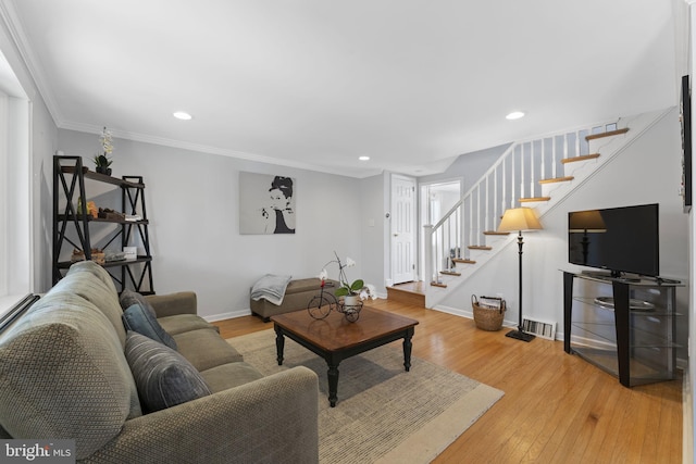 living room featuring crown molding, light wood finished floors, visible vents, baseboards, and stairs