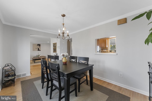 dining space featuring ornamental molding, light wood-style flooring, visible vents, and an inviting chandelier