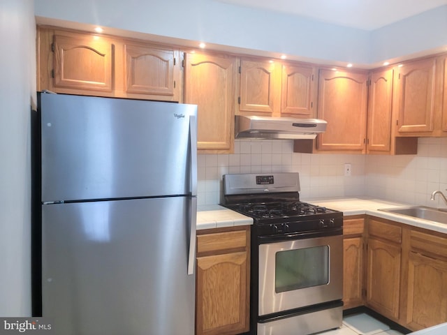 kitchen featuring tasteful backsplash, stainless steel appliances, under cabinet range hood, a sink, and tile countertops