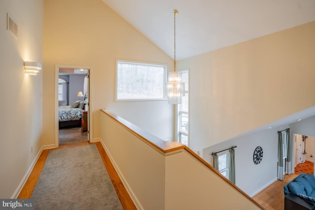 hallway featuring visible vents, an upstairs landing, an inviting chandelier, wood finished floors, and high vaulted ceiling