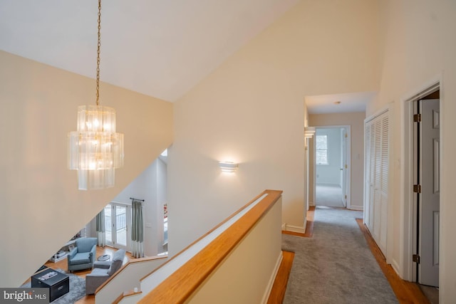 hallway with an upstairs landing, high vaulted ceiling, carpet, and an inviting chandelier