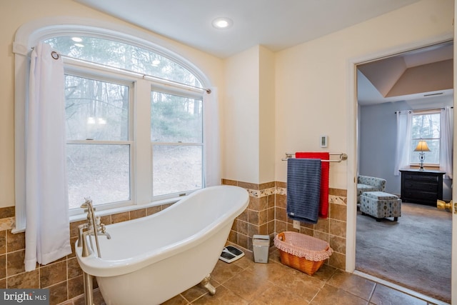 bathroom with tile walls, a freestanding tub, a healthy amount of sunlight, and a wainscoted wall