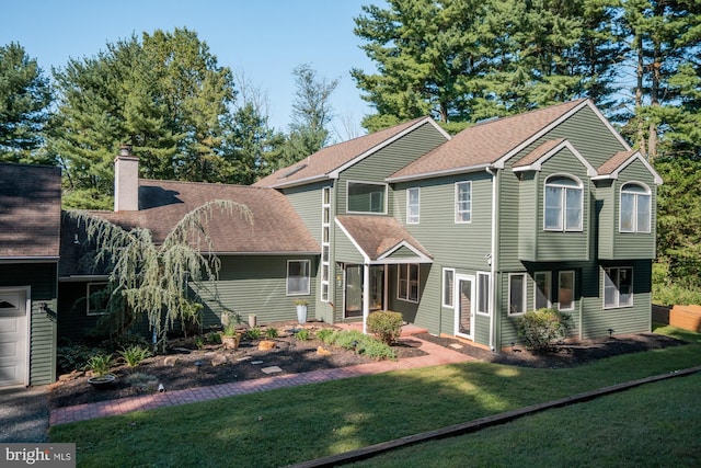 rear view of property featuring a lawn, roof with shingles, and a chimney