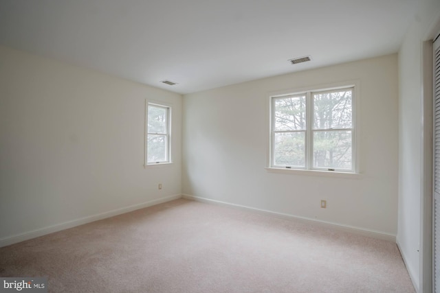 unfurnished bedroom with visible vents, multiple windows, and light colored carpet