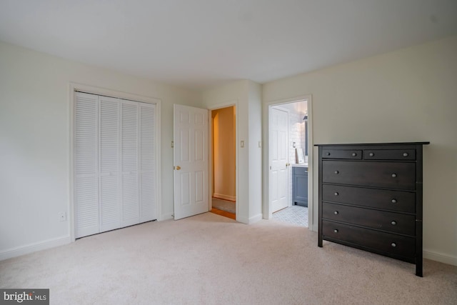 unfurnished bedroom with ensuite bath, baseboards, a closet, and light carpet