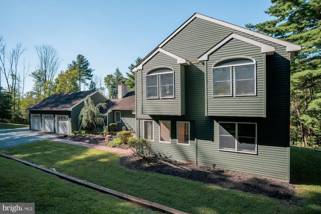 view of front facade featuring an outbuilding, a garage, a chimney, and a front lawn