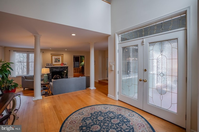 entryway featuring decorative columns, wood finished floors, a fireplace, and french doors