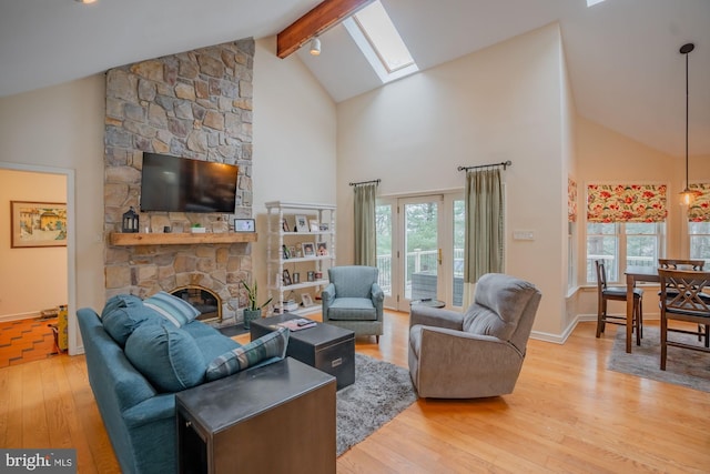 living room featuring baseboards, beam ceiling, a stone fireplace, a skylight, and wood finished floors