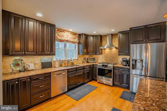 kitchen with a sink, tasteful backsplash, appliances with stainless steel finishes, wall chimney exhaust hood, and light wood finished floors