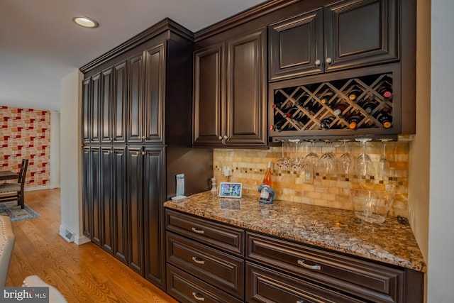 kitchen with light stone counters, light wood-type flooring, backsplash, and dark brown cabinetry