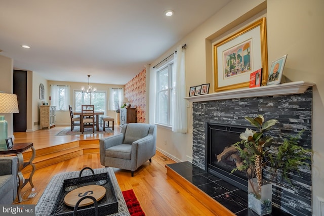 living area with baseboards, a tiled fireplace, recessed lighting, wood finished floors, and a notable chandelier