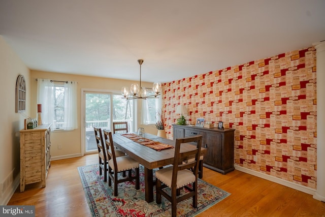 dining area with light wood-type flooring, baseboards, and an inviting chandelier