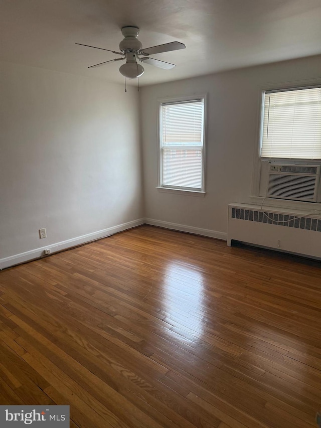 empty room featuring cooling unit, wood finished floors, a ceiling fan, baseboards, and radiator heating unit