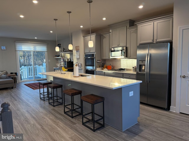 kitchen featuring a breakfast bar area, stainless steel appliances, light countertops, an island with sink, and pendant lighting