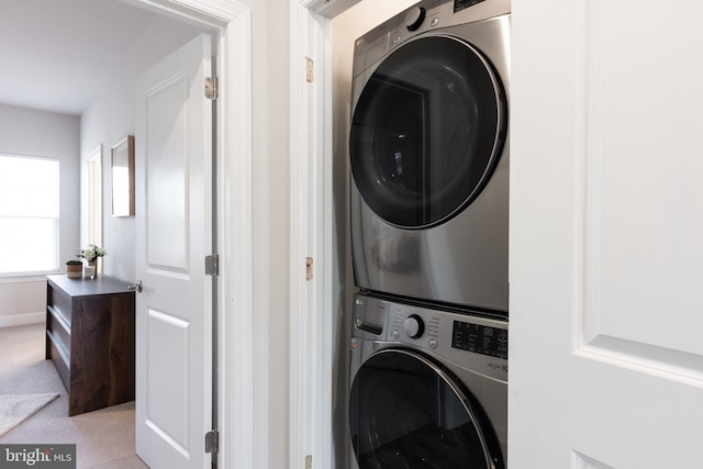 laundry area featuring light carpet, laundry area, baseboards, and stacked washer / drying machine