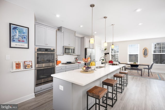 kitchen with pendant lighting, a center island with sink, a breakfast bar area, stainless steel appliances, and light countertops