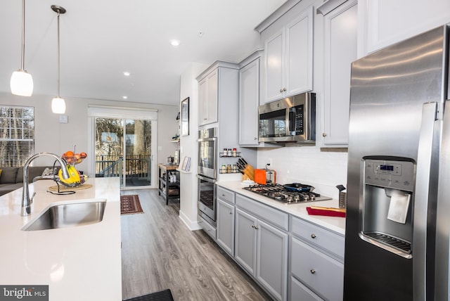 kitchen featuring appliances with stainless steel finishes, hanging light fixtures, light countertops, gray cabinetry, and a sink