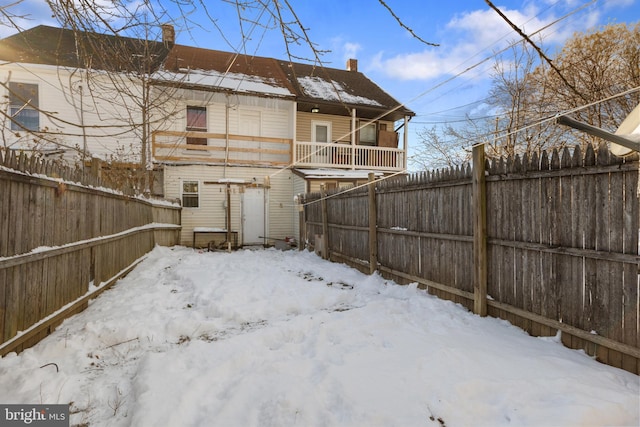 snow covered rear of property featuring a fenced backyard and a chimney