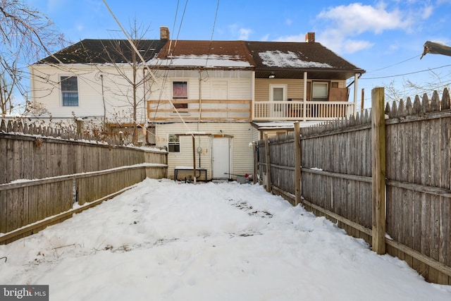 snow covered house with a chimney and a fenced backyard