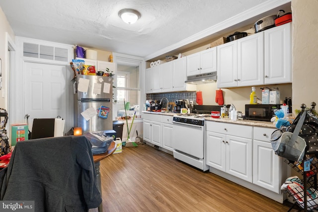 kitchen with light countertops, freestanding refrigerator, white gas stove, and white cabinets