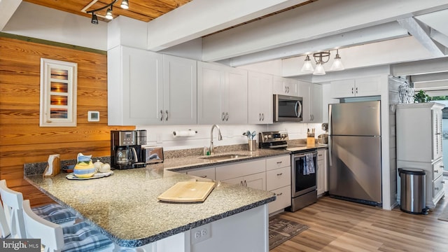 kitchen with white cabinets, a peninsula, stainless steel appliances, a kitchen bar, and a sink