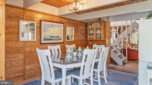 dining room featuring wooden ceiling, wood walls, wood finished floors, stairway, and an inviting chandelier