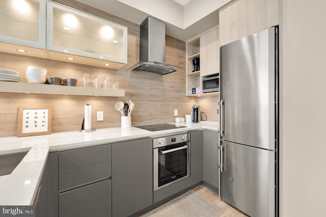 kitchen featuring gray cabinetry, stainless steel appliances, light hardwood / wood-style flooring, wall chimney range hood, and decorative backsplash