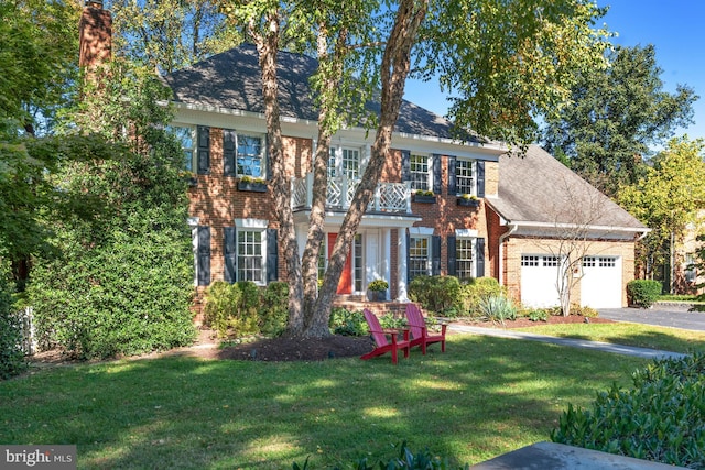 view of front facade with brick siding, a balcony, roof with shingles, an attached garage, and a front yard