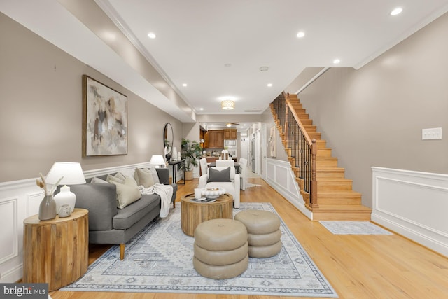 living room featuring light wood finished floors, ornamental molding, stairs, a decorative wall, and recessed lighting