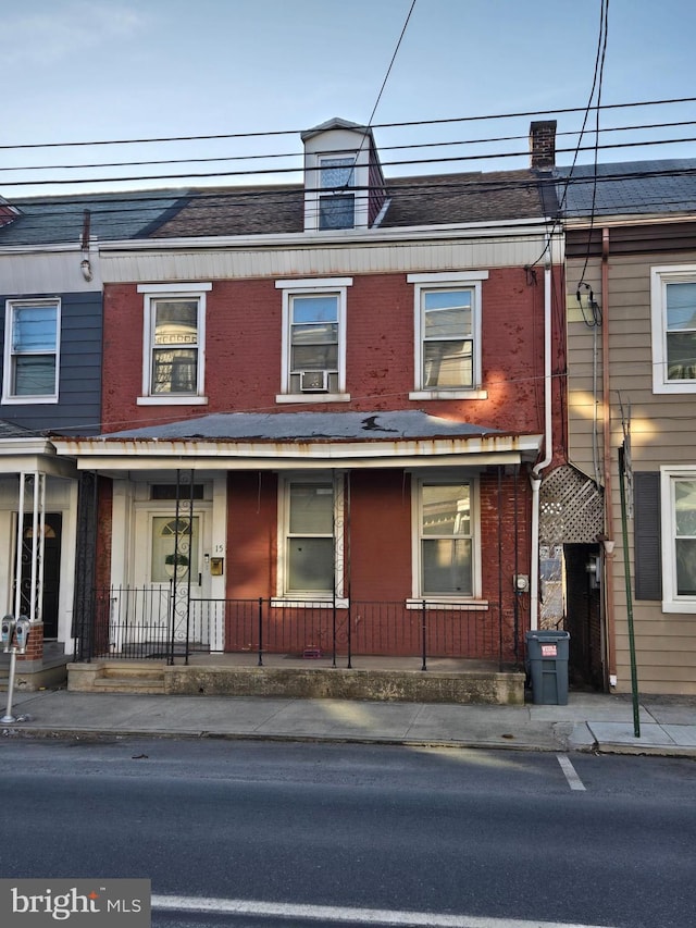 townhome / multi-family property featuring covered porch, a shingled roof, mansard roof, and brick siding