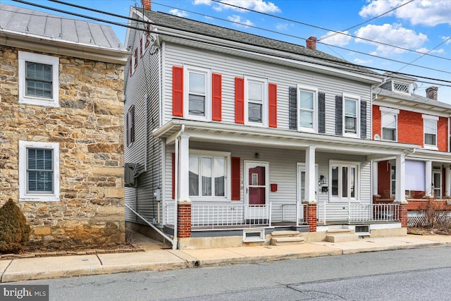 townhome / multi-family property with stone siding, a chimney, metal roof, a standing seam roof, and a porch