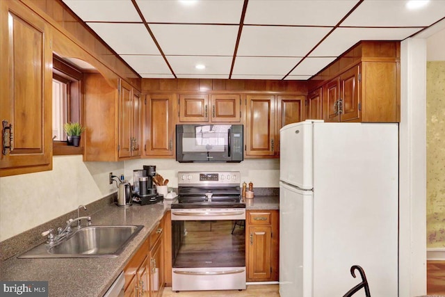 kitchen featuring brown cabinets, freestanding refrigerator, stainless steel range with electric cooktop, a sink, and black microwave