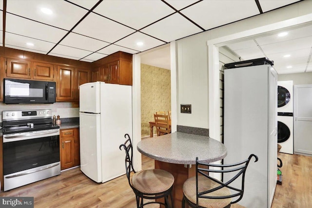 kitchen with electric range, stacked washer / dryer, dark countertops, freestanding refrigerator, and black microwave