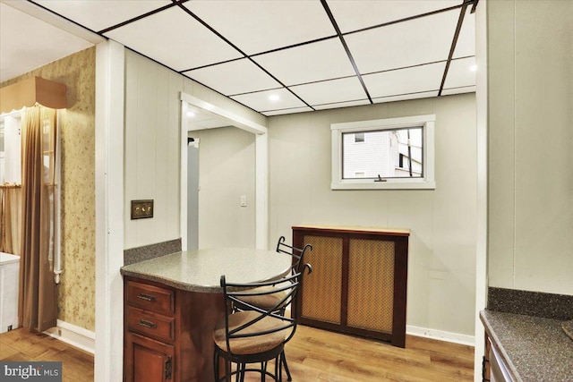 bar featuring baseboards, a drop ceiling, and light wood-style floors