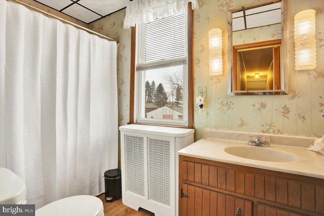 bathroom with radiator, wallpapered walls, toilet, and vanity