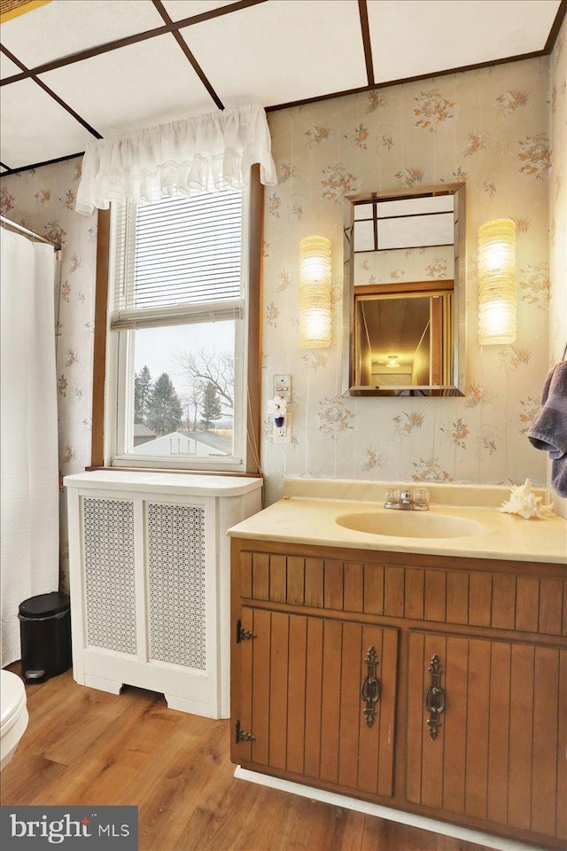 bathroom featuring radiator, toilet, vanity, wood finished floors, and wallpapered walls