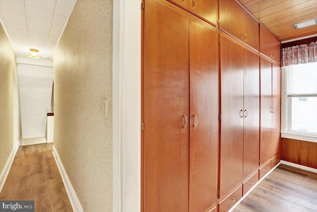 corridor featuring light wood-style floors, baseboards, and a textured wall