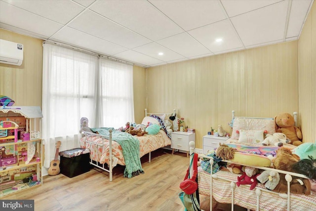 bedroom featuring an AC wall unit, wood finished floors, and a paneled ceiling