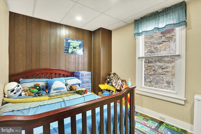 bedroom featuring a drop ceiling, baseboards, and wallpapered walls