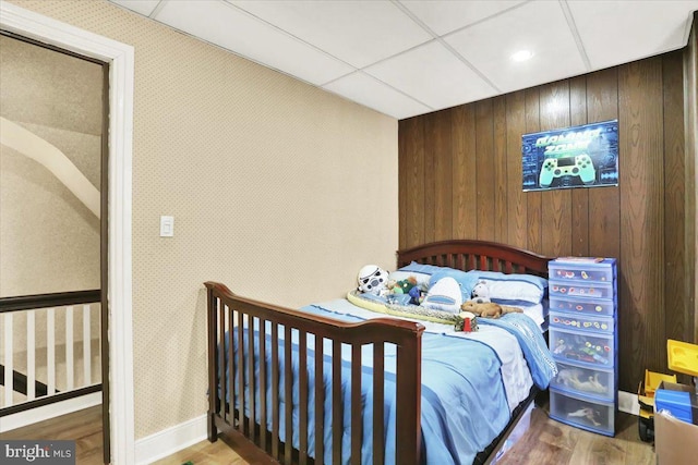 bedroom with a paneled ceiling, wallpapered walls, and wood finished floors