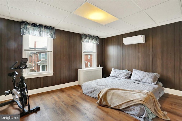 bedroom with wooden walls, a wall mounted air conditioner, wood finished floors, and radiator