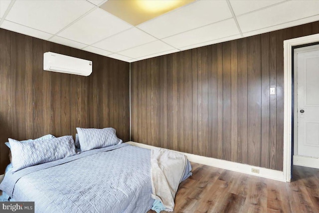 bedroom featuring baseboards, dark wood-style floors, a wall mounted air conditioner, a paneled ceiling, and wood walls