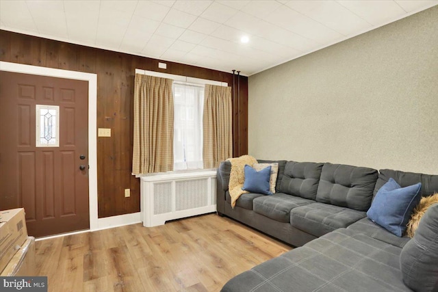 living room with radiator, baseboards, wooden walls, and light wood finished floors