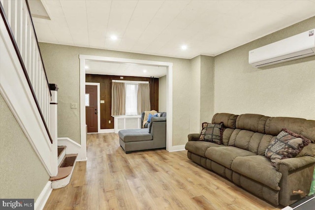 living room with baseboards, a wall mounted air conditioner, light wood finished floors, and stairs