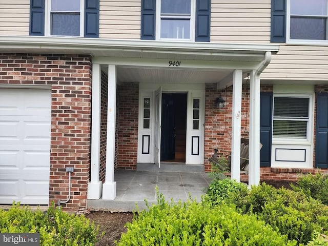 doorway to property with a garage and brick siding