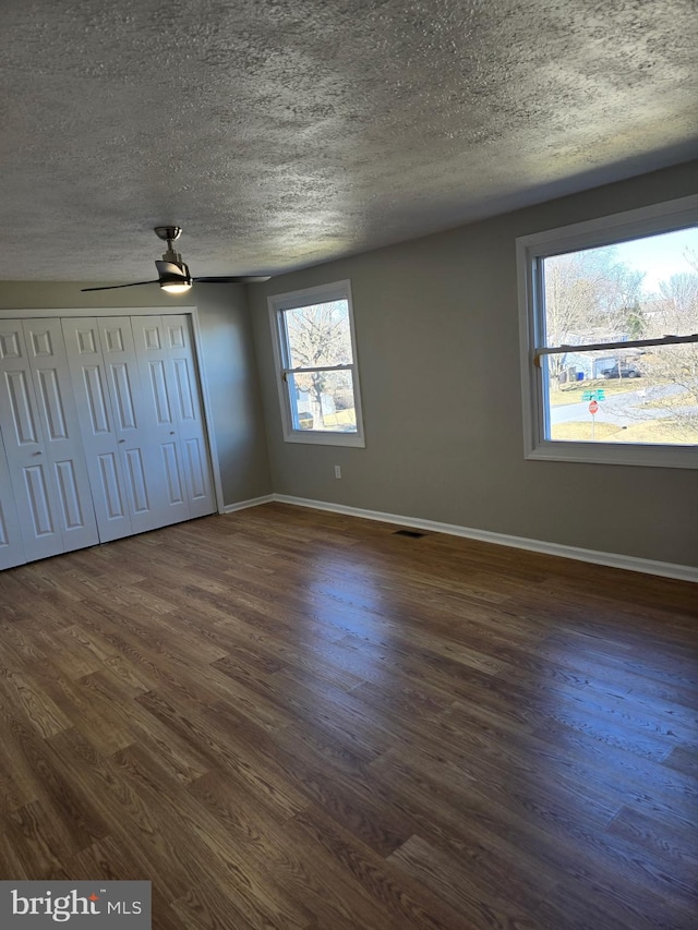 unfurnished bedroom featuring dark wood-style floors, visible vents, baseboards, and a textured ceiling