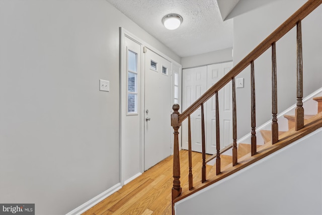 entrance foyer with light wood-type flooring, a textured ceiling, baseboards, and stairs