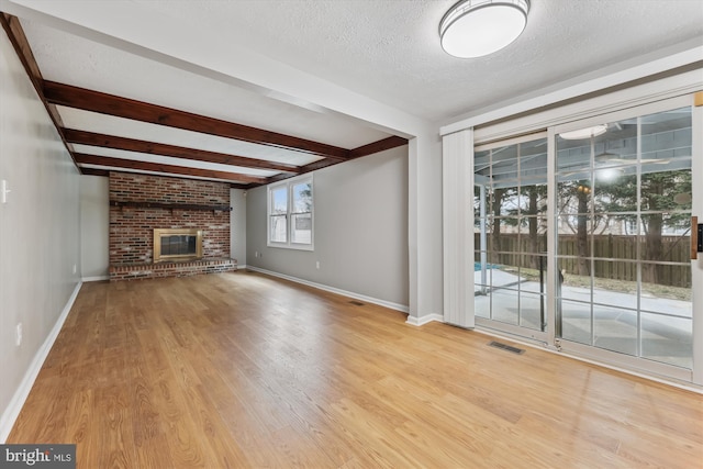 unfurnished living room featuring light wood-type flooring, a fireplace, visible vents, and a textured ceiling