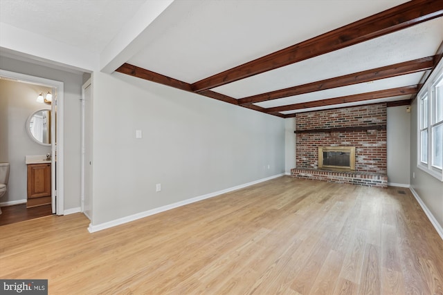 unfurnished living room featuring a brick fireplace, baseboards, light wood finished floors, and beamed ceiling